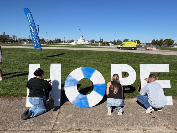 Walkers, seen from behind, writing messages on giant white HOPE letters on the lawn at the Out of the Darkness Walk on Belle Isle