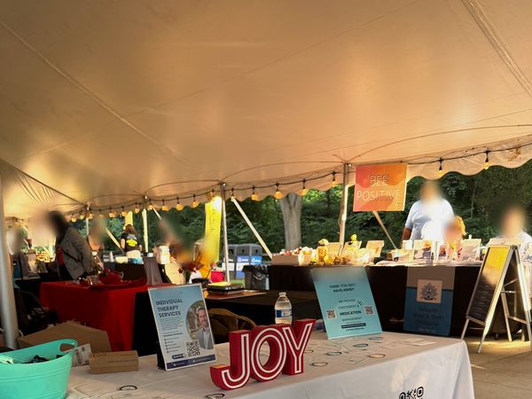 Wide view of the Joy Mental Health Group outreach booth under a white tent at ViewFest at the Detroit Zoo, with JOY letters on the table